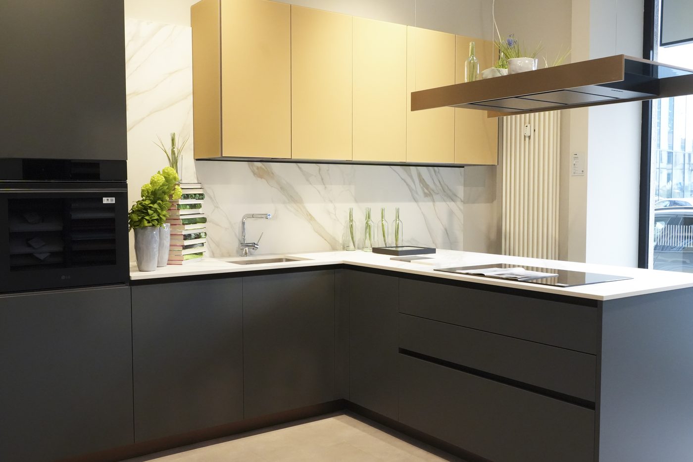 Cucina ad angolo con basi scure, pensili champagne e schienale effetto marmo
